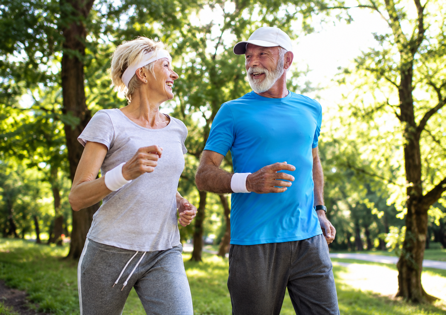 Smiling elderly couple jogging together in a sunny park with trees in the background.